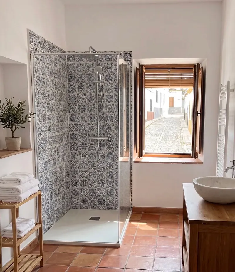 Bathroom with patterned blue tiles, walk-in shower and terracotta floor